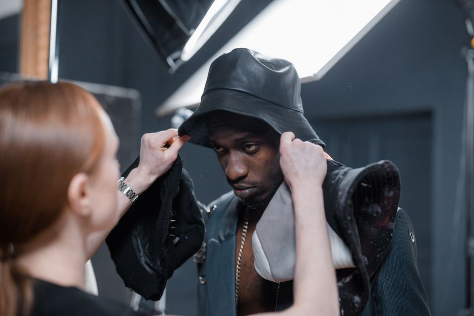 A stylist adjusts a model's outfit during a photoshoot in a studio setting.