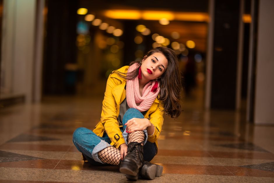 Fashionable woman in a yellow coat and pink scarf posing indoors, exuding modern style and confidence.
