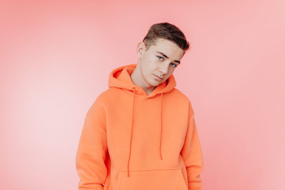 Portrait of a teenager in an orange hoodie posing against a vibrant pink background.