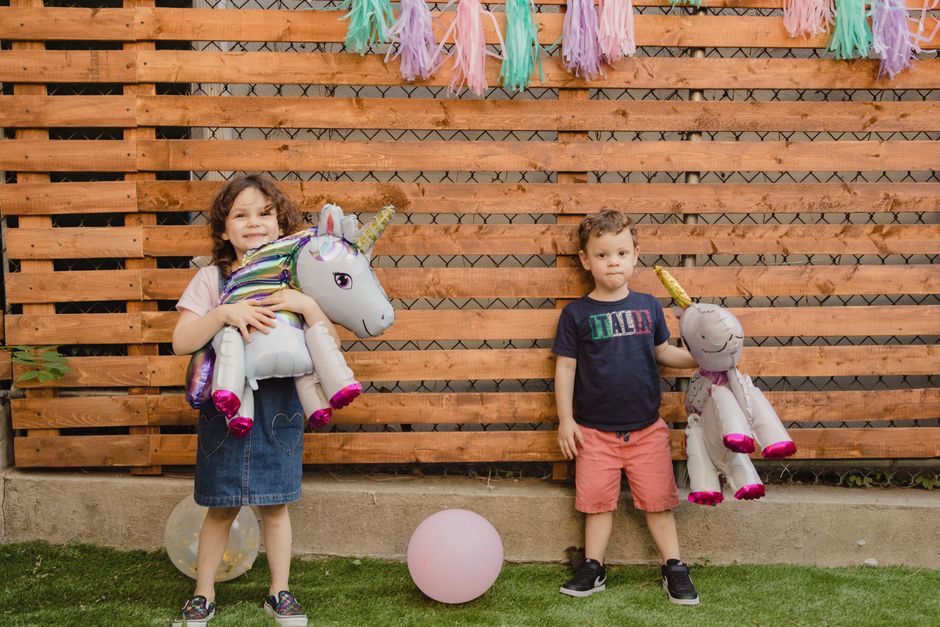 Two children holding unicorn balloons at an outdoor party with decorations.