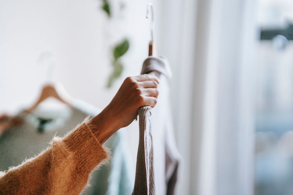 Crop unrecognizable female in sweater holding hanger with shirt while choosing clothes for work