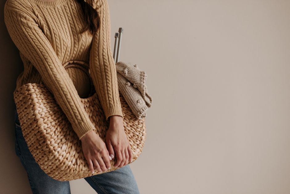 Close-up image of a person in a knitted sweater holding a stylish woven basket, offering a cozy autumn vibe.
