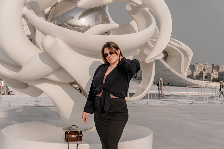 Fashionable woman posing by a modern sculpture outdoors in daylight.