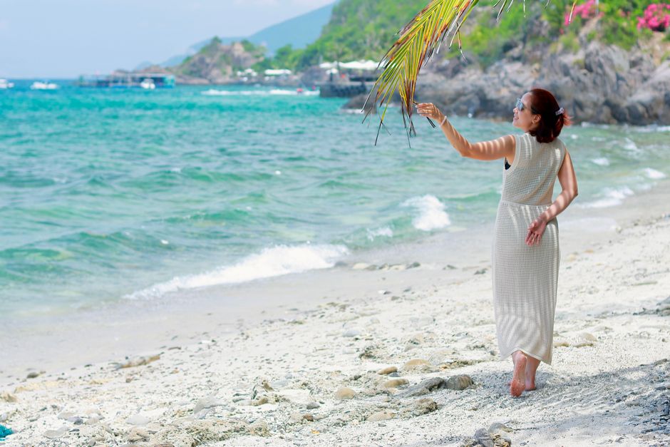 A woman in a white dress enjoys a sunny day on a tropical beach with clear blue waters.