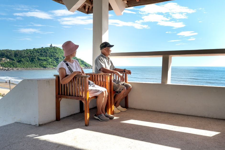 Senior couple sitting on balcony chairs, enjoying a relaxing ocean view in summer.