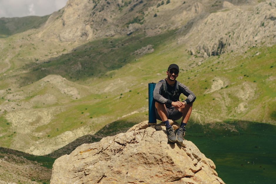A solo hiker sits on a rock enjoying the scenic mountain landscape on a sunny day.