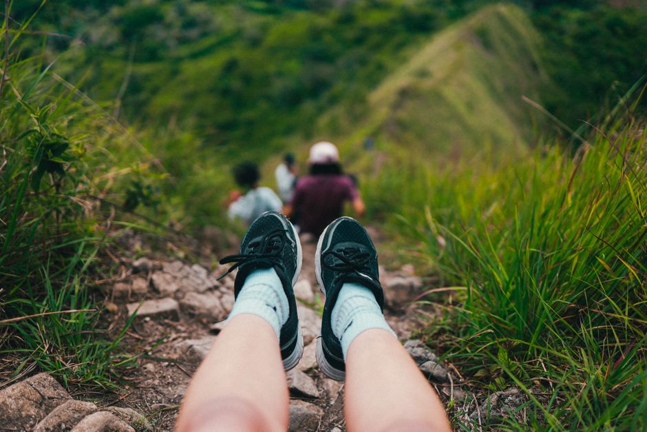 A person enjoys a hillside view, wearing sneakers on a hiking trail surrounded by greenery.