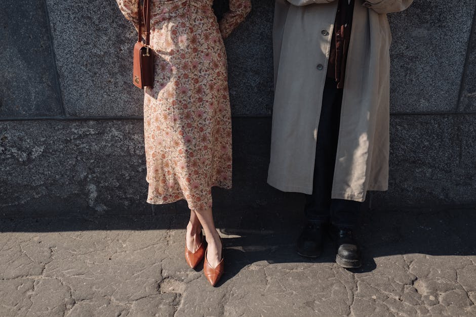 A fashionable couple stands outdoors against a stone wall, showcasing chic outerwear.