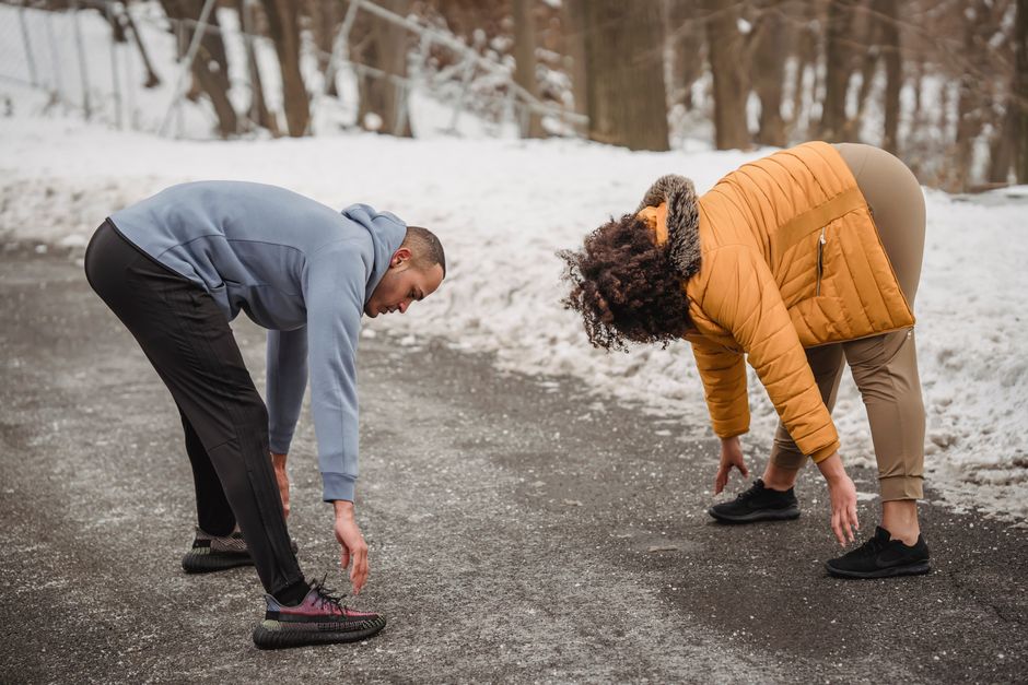 Full body side view of active African American couple bending forward while doing stretching exercise on asphalt walkway during training in winter time