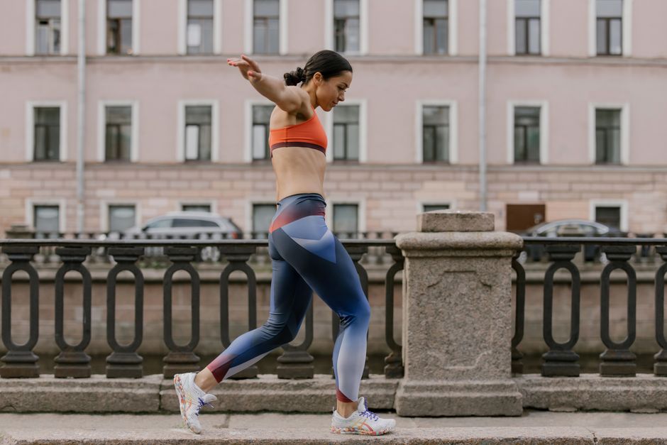 Woman in colorful activewear balancing on a sidewalk in front of a classic building.