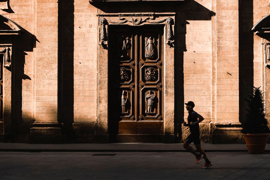 A jogger runs past ornate wooden doors of a historic church at sunset, casting long shadows.