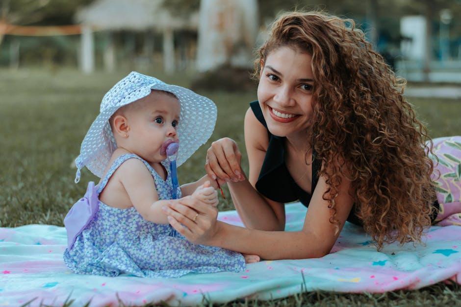 Smiling mother and baby girl bonding while lying on a colorful blanket outdoors.