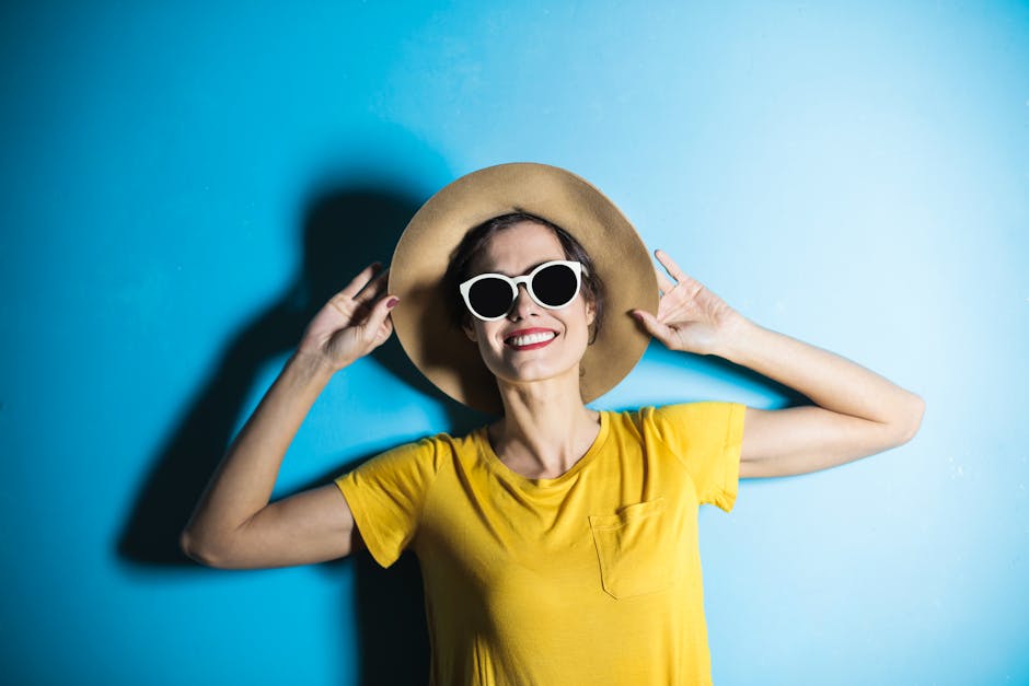 Smiling woman in yellow t-shirt and sun hat posing against a vibrant blue background.