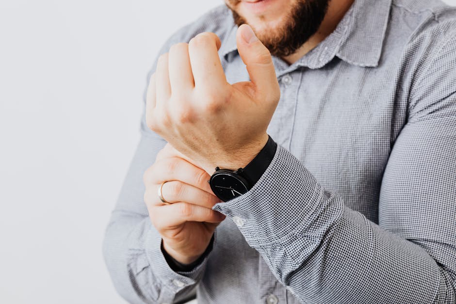 Man in gray shirt adjusting his wristwatch, focusing on the details of the watch and sleeve.
