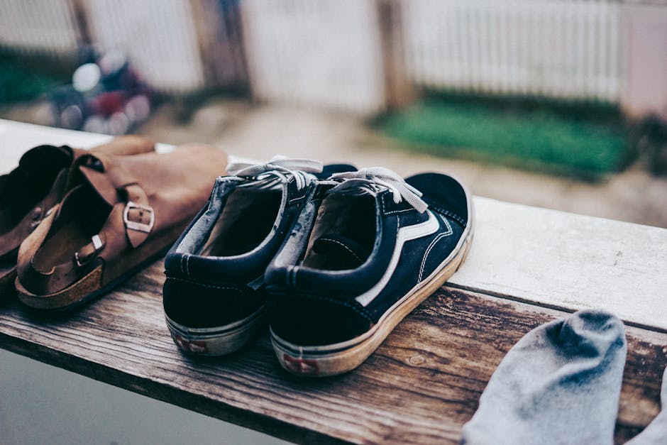 Close-up of casual sneakers and sandals drying on a wooden balcony ledge.