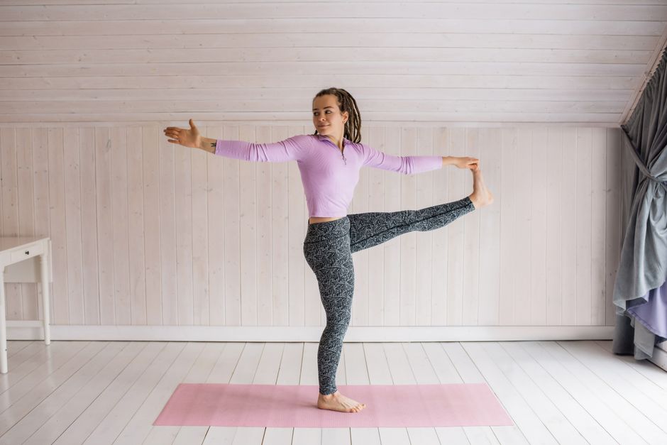 Woman practicing a yoga balance pose on a mat indoors, enhancing flexibility.