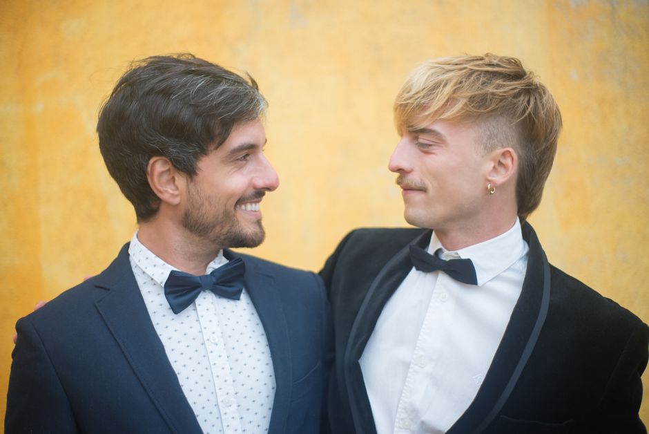 Charming gay couple in elegant suits sharing a joyful moment outdoors.