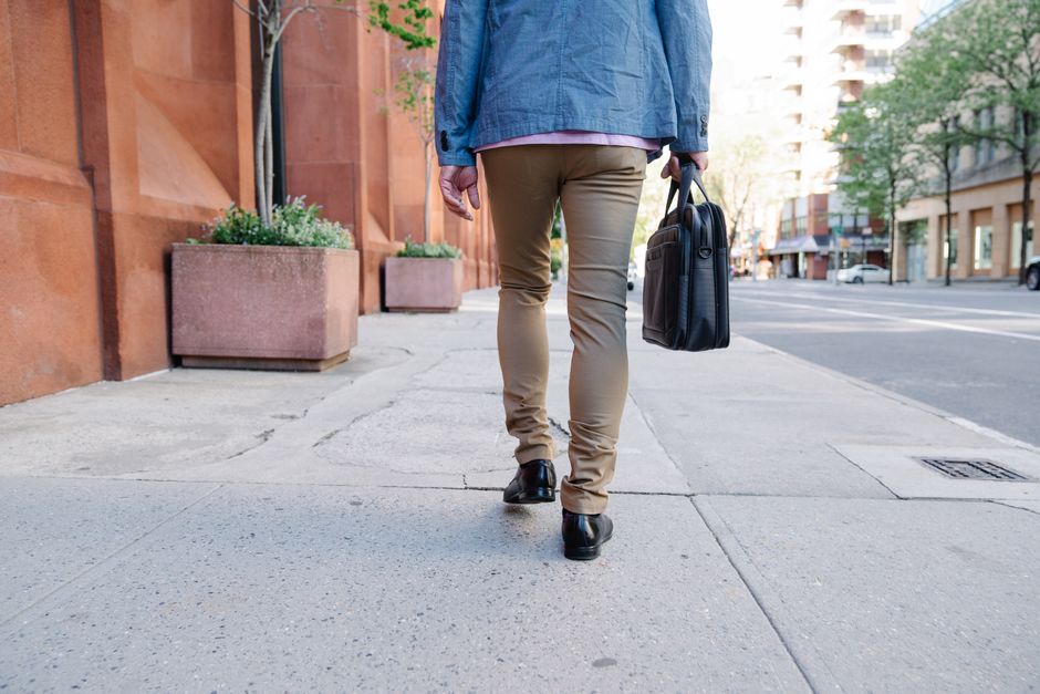 Rear view of a person walking on a city sidewalk holding a briefcase, embodying urban lifestyle.