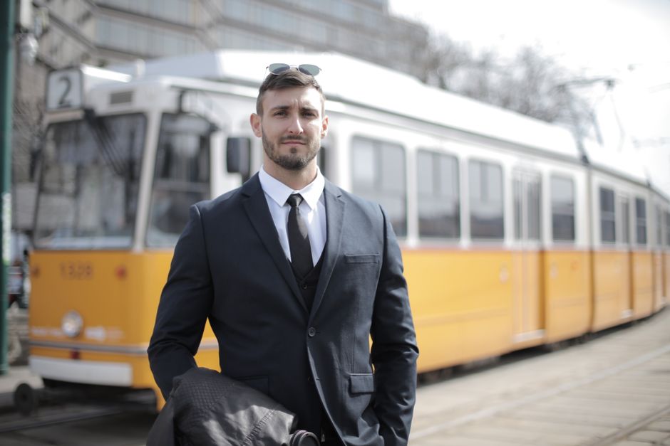 Confident businessman in formal suit standing by a yellow tram in an urban setting.