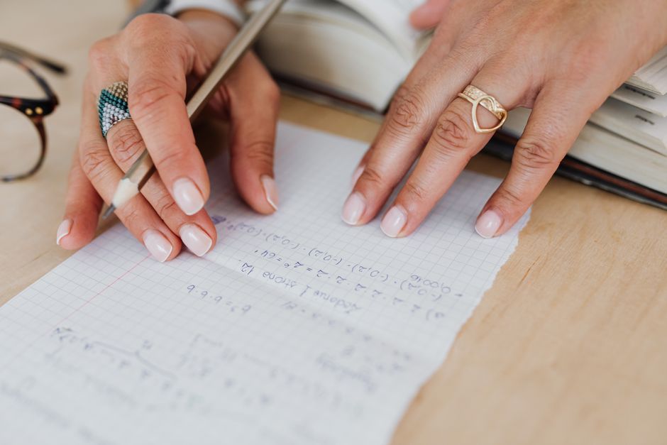 A woman writes mathematical formulas on graph paper, showcasing precision and focus.