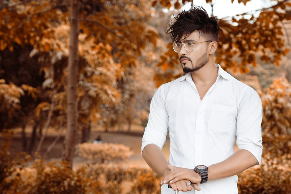 A fashionable man with glasses in an outdoor autumn setting wearing a white shirt.