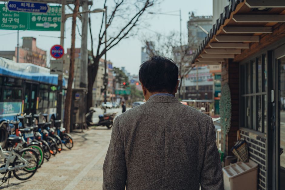 A man in a suit walks through a bustling street in Seoul, capturing urban life.
