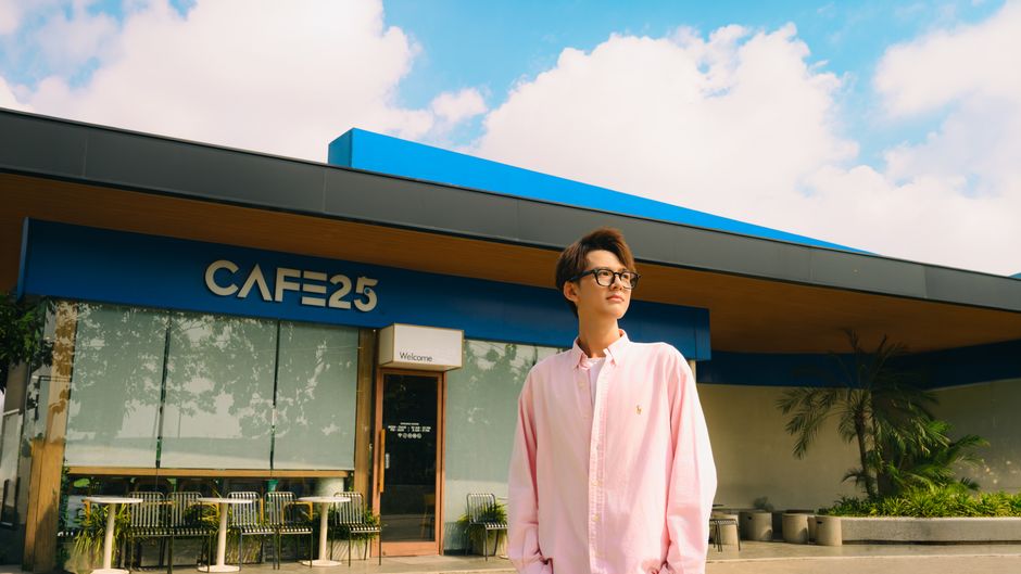 Stylish young man in glasses standing outside Café 25 on a sunny day.