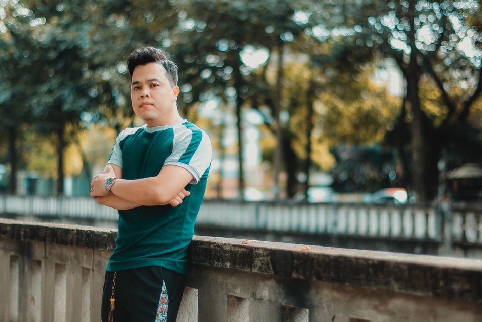 Man standing confidently by a railing outdoors with trees in the background.