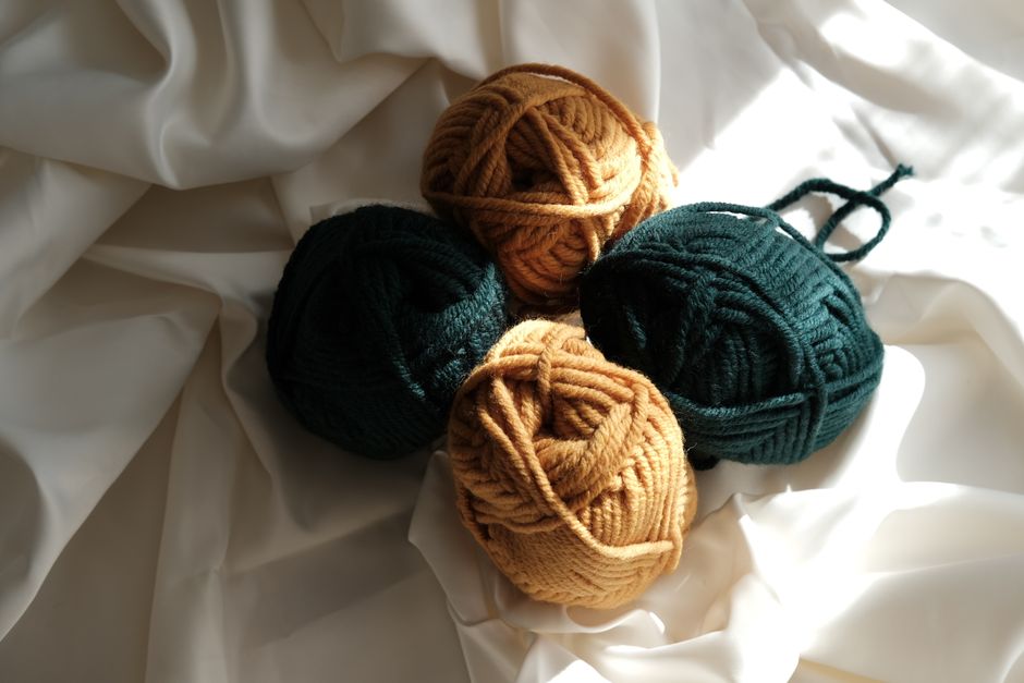Four yarn balls in earth tones on white fabric in natural lighting, top view.