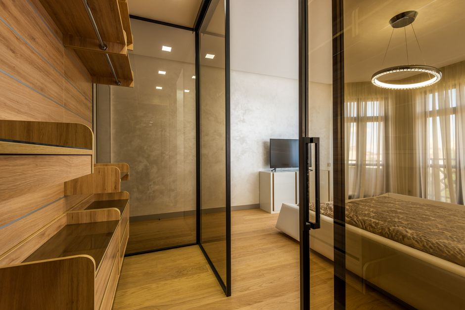 Modern empty wardrobe with glass doors and wooden shelves placed in spacious bedroom in contemporary flat