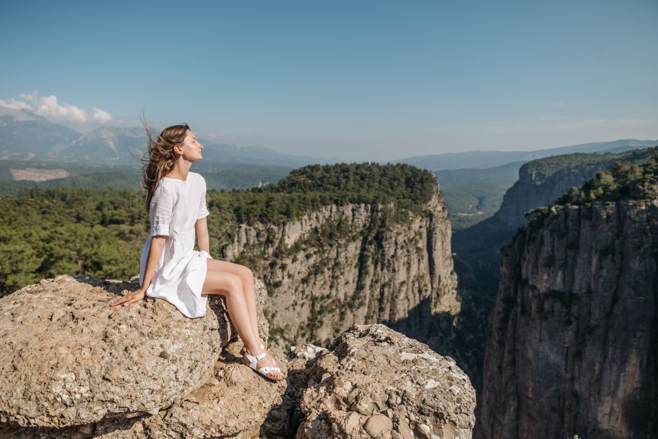 Woman in white dress sitting on a cliff overlooking a stunning canyon landscape.