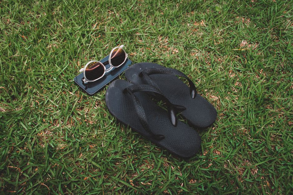 Casual black flip-flops and sunglasses resting on a lush green lawn on a sunny day.