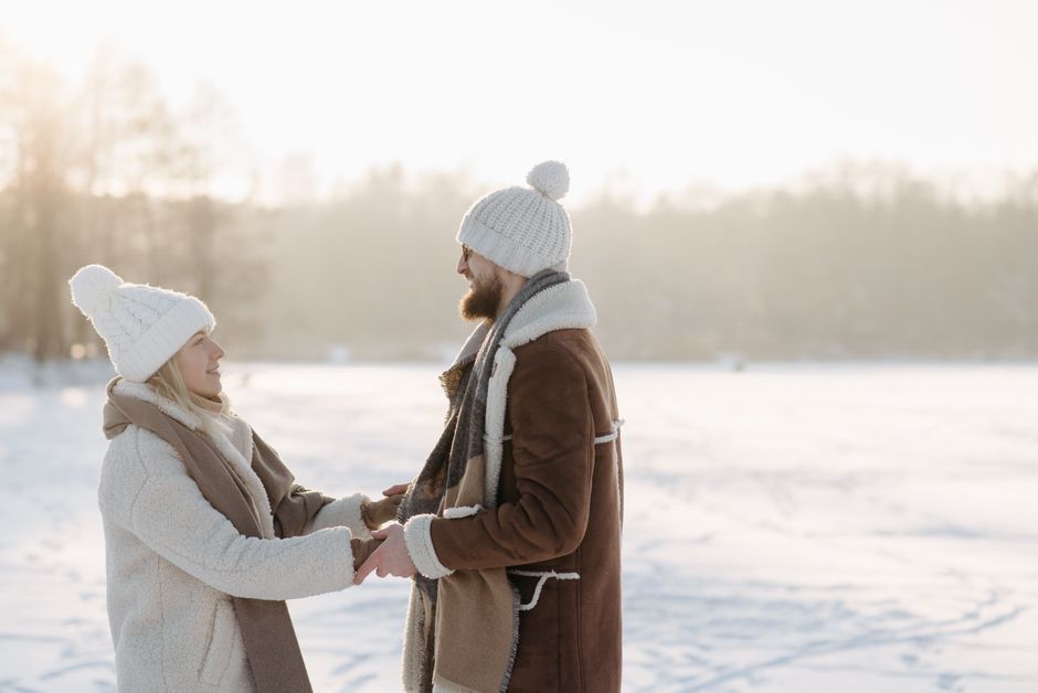 Happy couple in winter clothing holding hands in a snowy landscape, expressing love.