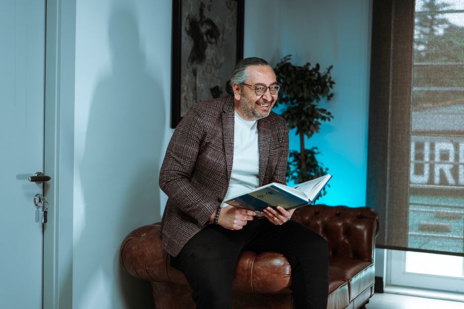 Smiling adult man sits on a leather sofa enjoying a book in a stylish, cozy indoor setting.