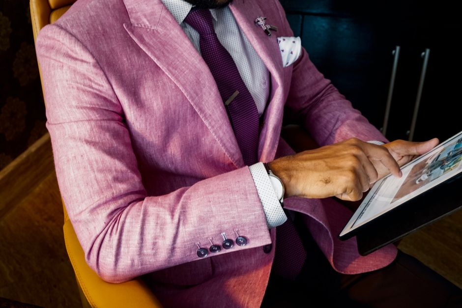A fashionable businessman in a pink suit uses a tablet in a modern office setting.