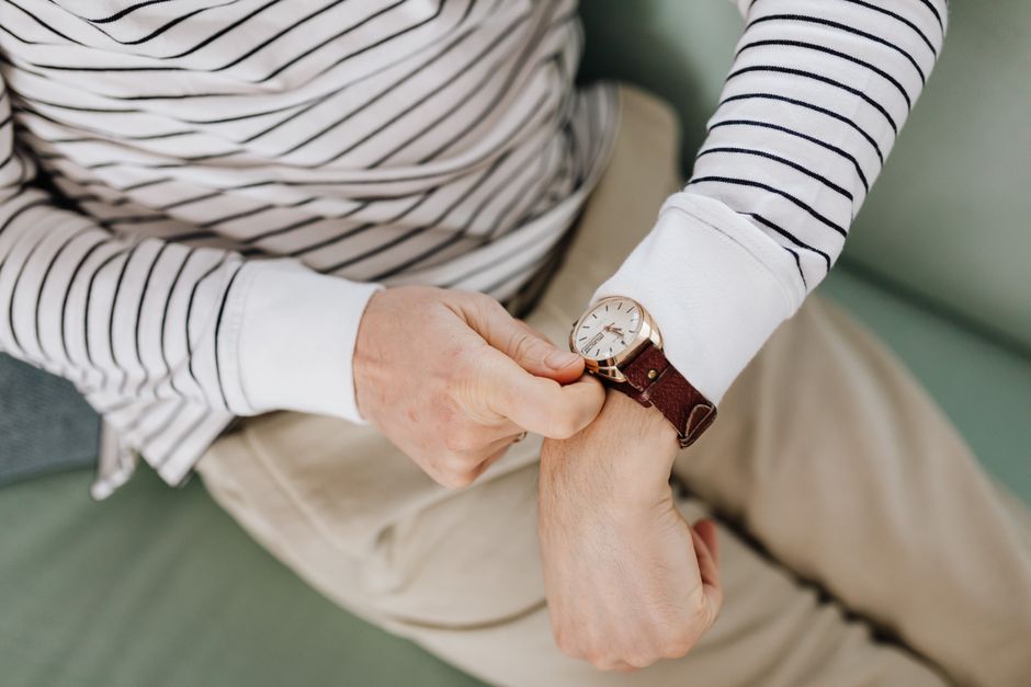 Close-up of a man adjusting his wristwatch over a striped long sleeve shirt.