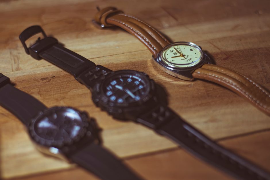 Three wristwatches with analog dials on a wooden surface showing leather and rubber straps.