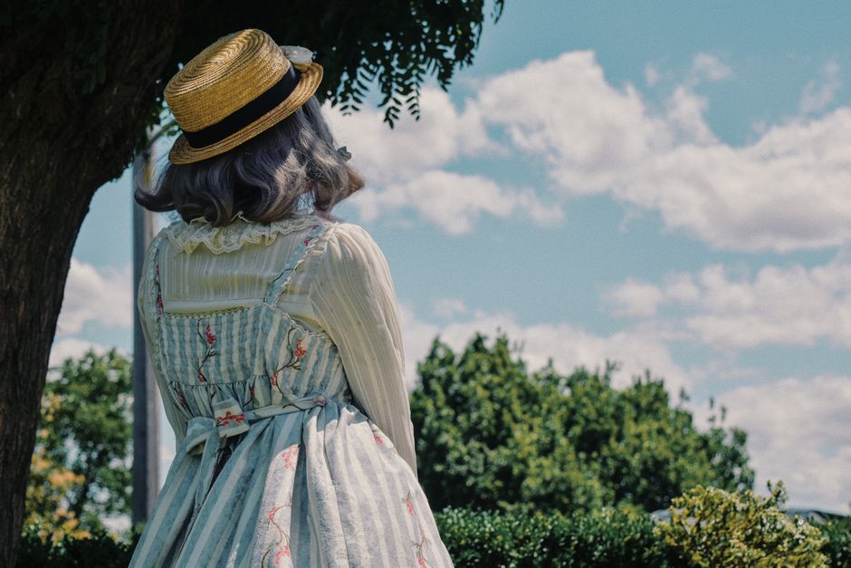 Back view of woman in vintage attire under a tree on a sunny day.