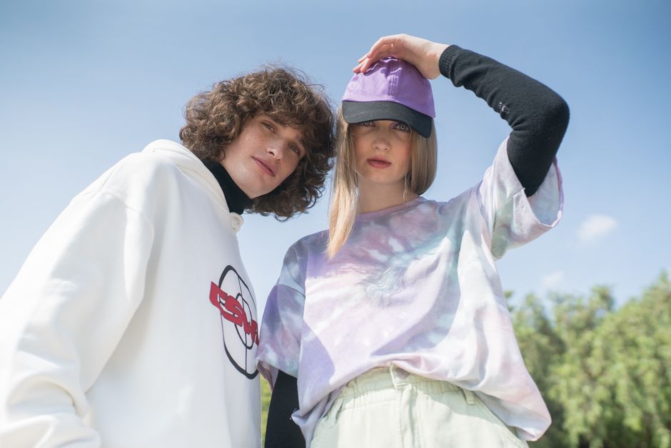 Young couple posing in colorful streetwear fashion, showcasing casual style with caps and hoodies outdoors.