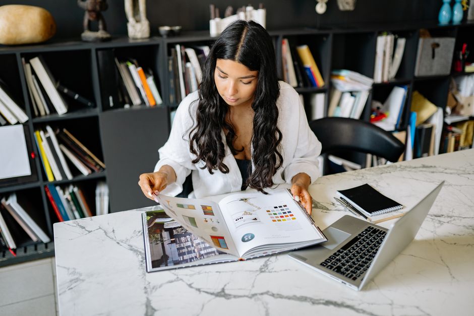 Young woman studying design concepts in a modern office setting with a laptop and books.