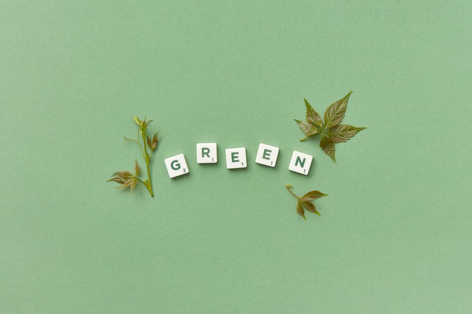 Green scrabble tiles forming the word 'GREEN' with leaves on green background.
