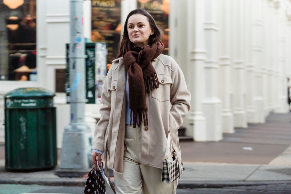 Positive female walking with hand in pocket on sidewalk and carrying bags during shopping in city