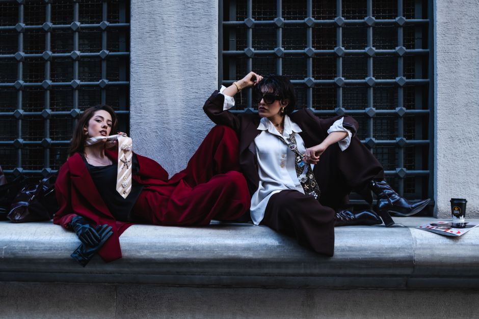 Two stylish women pose in urban fashion against a city backdrop.