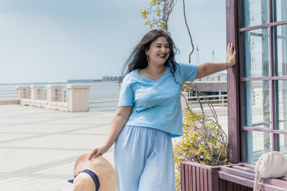 A smiling woman enjoys a sunny day at the Baku waterfront, wearing casual summer fashion.