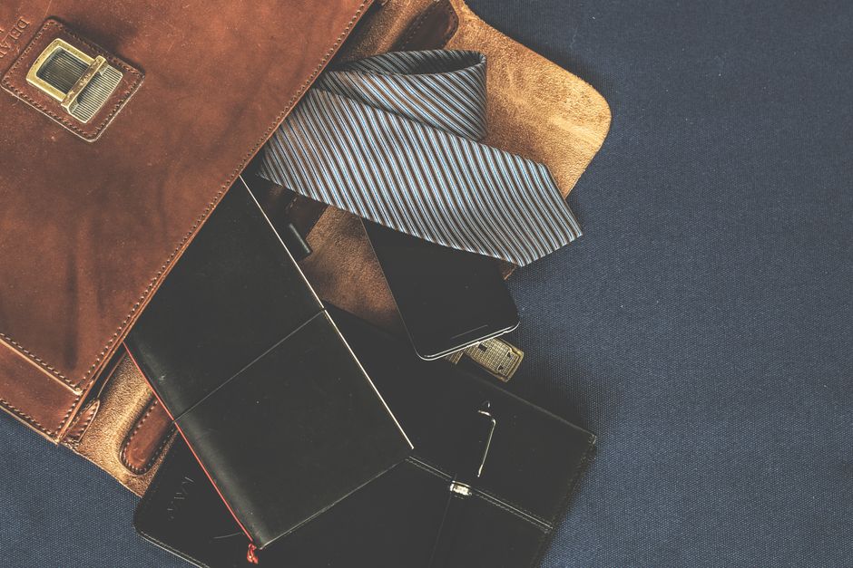 Flat lay of men's leather bag with accessories like a tie, notebook, and phone. Ideal for business themes.