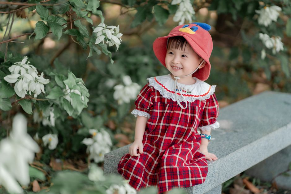 A smiling young child in a red dress enjoys a sunny day on a garden bench.