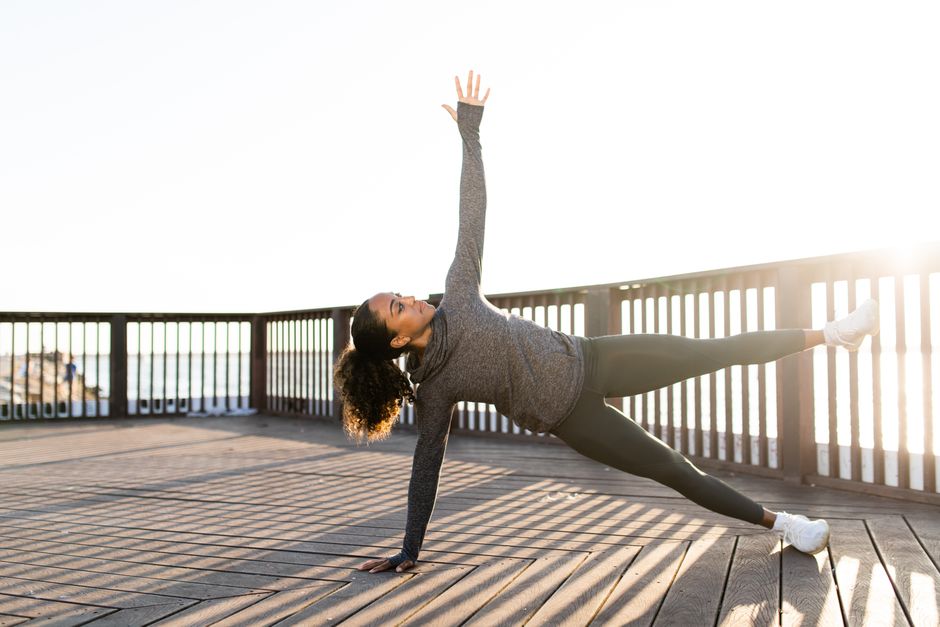African American woman doing yoga side plank on a sunny day outdoors. Focused and serene.