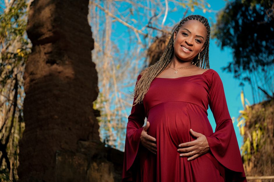 Joyful pregnant woman in red posing outdoors, enjoying the sunny day.