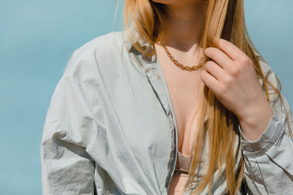 Close-up portrait of a woman in a light gray shirt and gold necklace, highlighting modern fashion.
