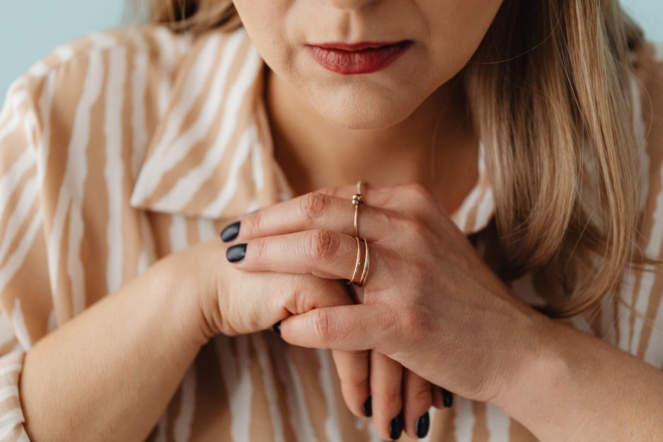 Close-up of a woman with clasped hands wearing rings, showing thoughtful expression.